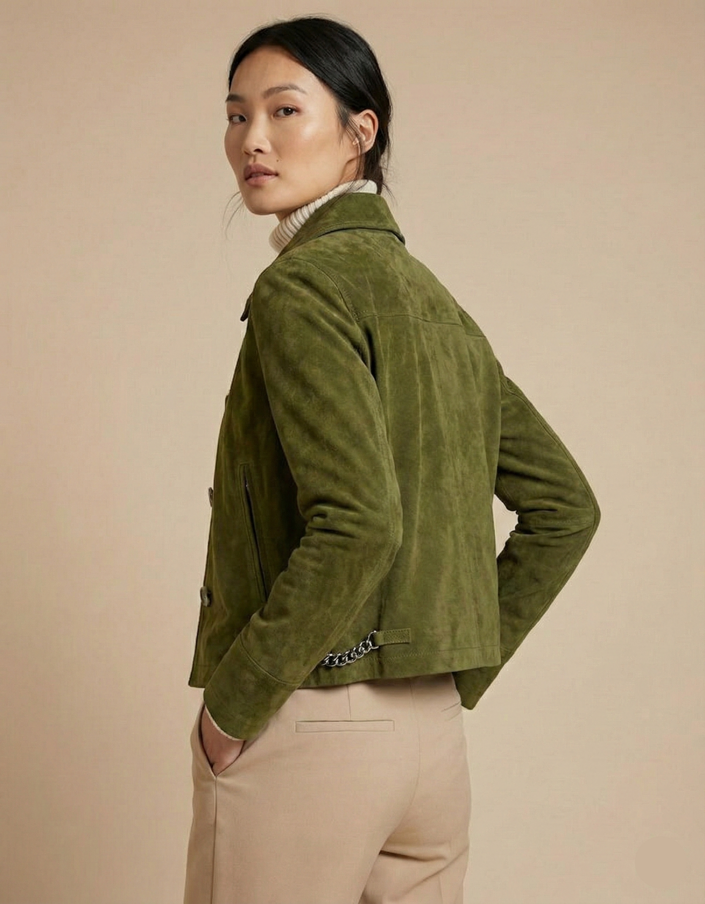 Woman wearing a green jacket and beige pants against a beige background