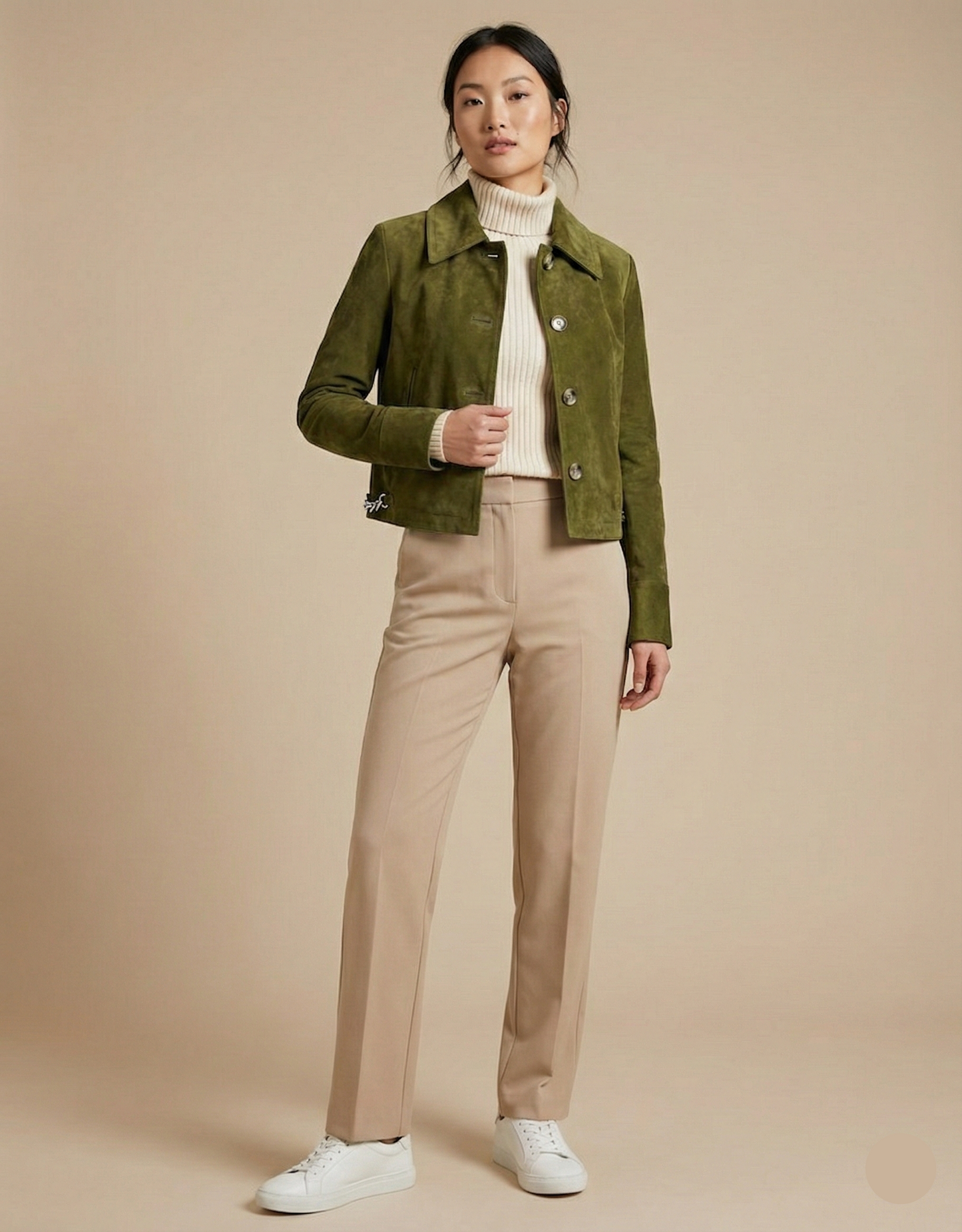Woman wearing a green jacket, white turtleneck, beige pants, and white sneakers on a beige background