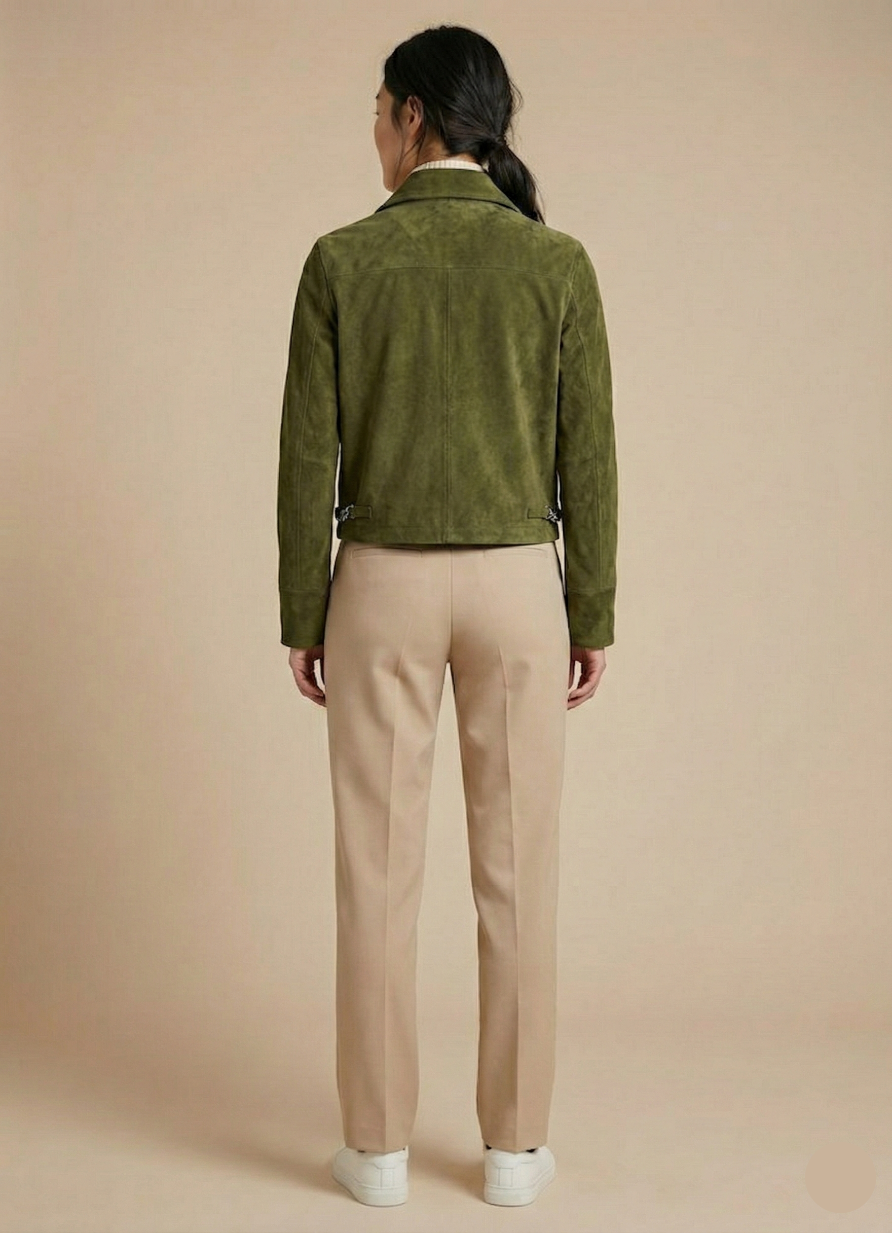 Person wearing a green jacket and beige pants on a beige background