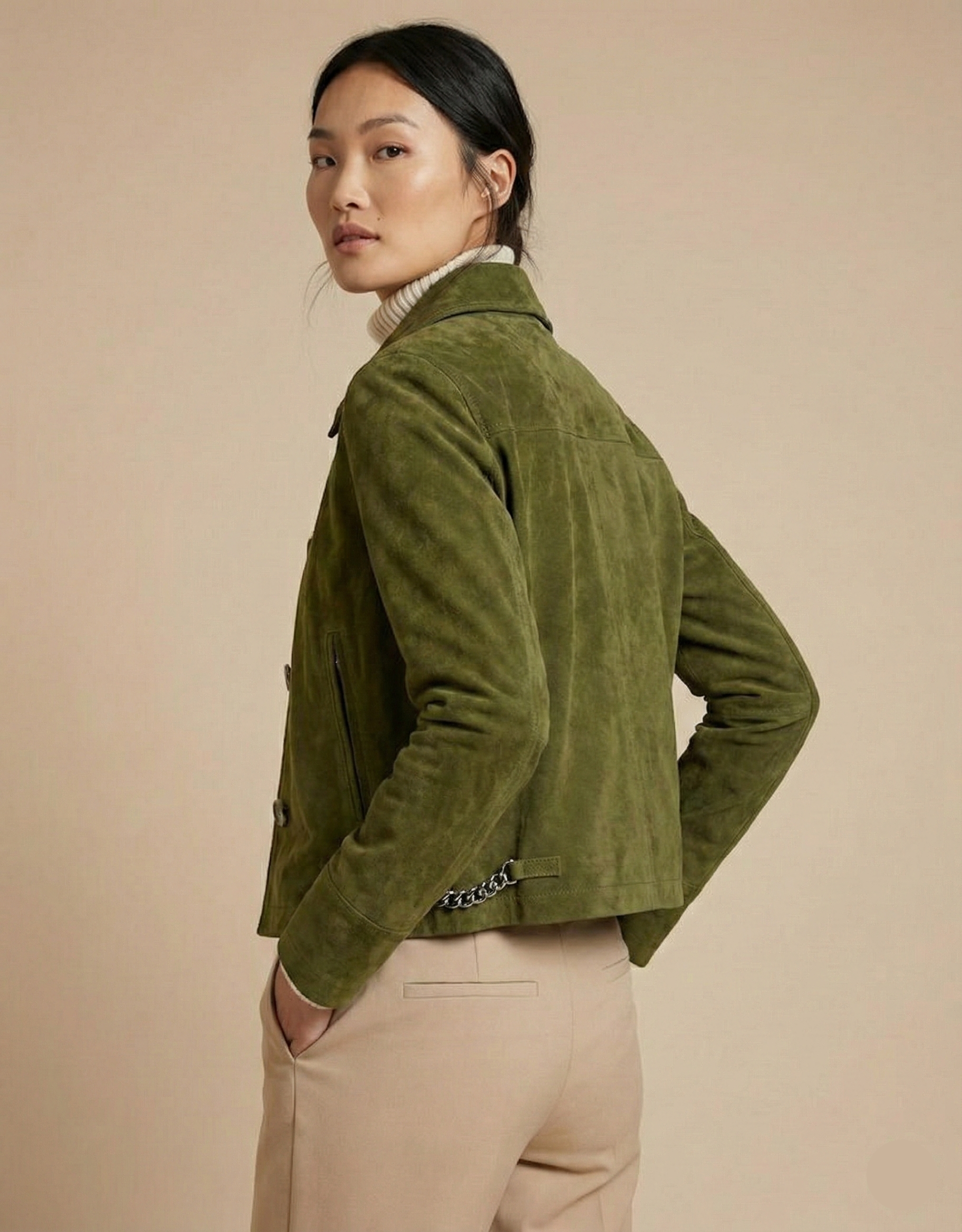 Woman wearing a green jacket and beige pants against a beige background
