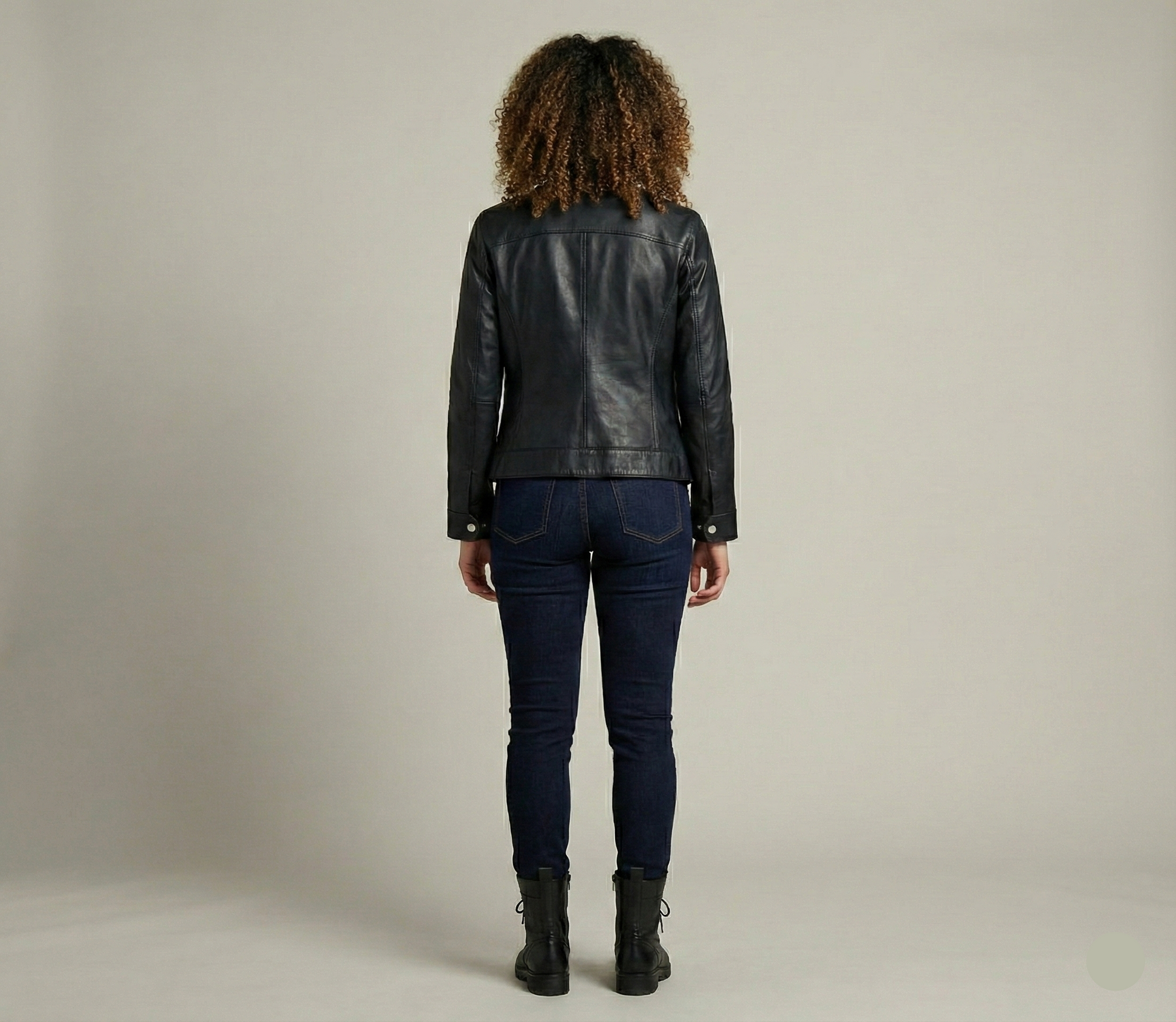 Person wearing a black leather jacket and dark jeans on a plain background