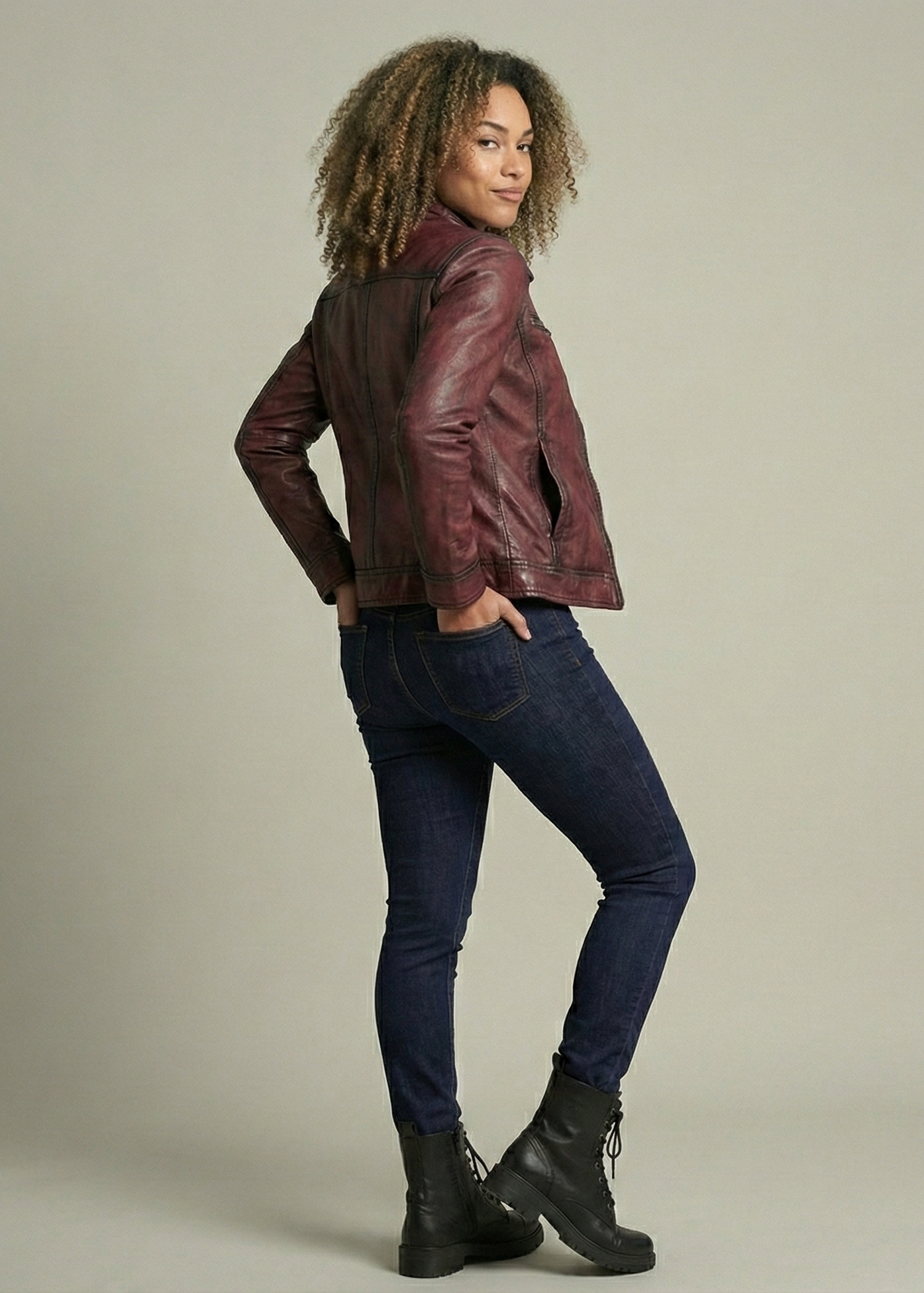 Person wearing a brown leather jacket, dark jeans, and black boots on a plain background