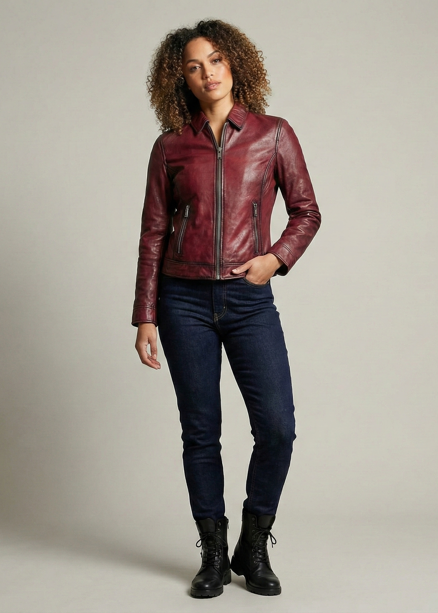 Woman wearing a red leather jacket and dark jeans against a neutral background